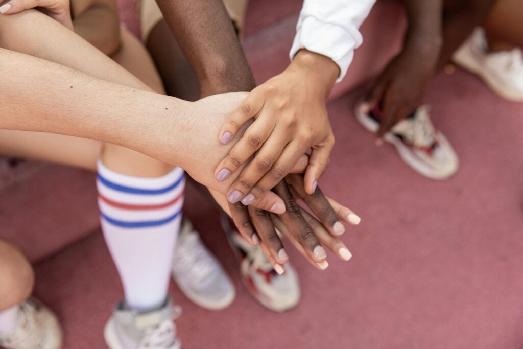 A group of friends stack their hands in unity on a sports court, symbolizing teamwork.
